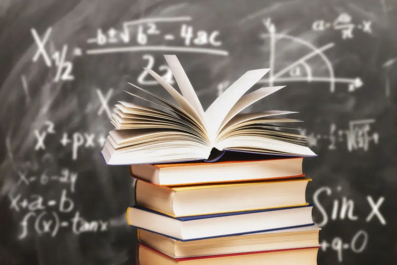 Stos książek z otwartą księgą na wierzchu na tle tablicy z równaniami matematycznymi.