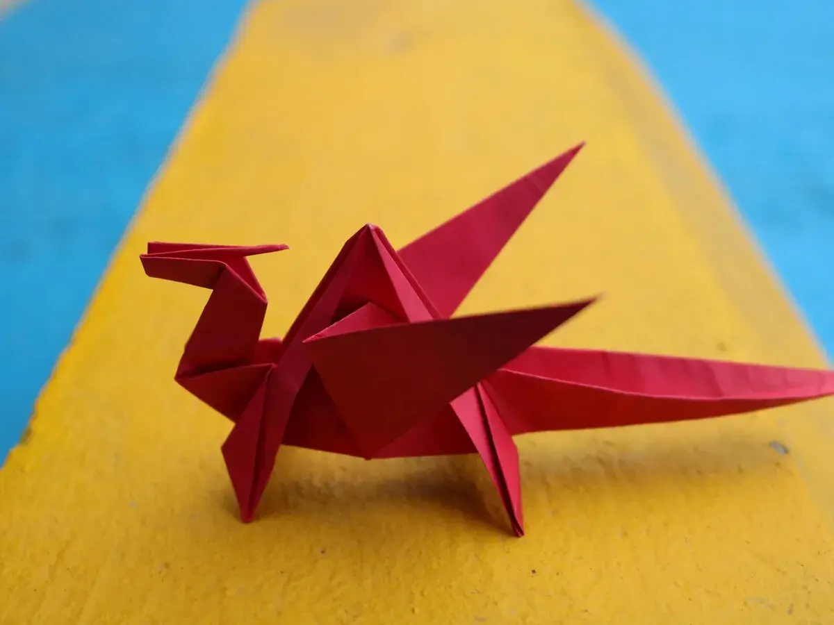 Un dragón rojo de papiroflexia fácil descansa sobre una superficie amarilla y azul.