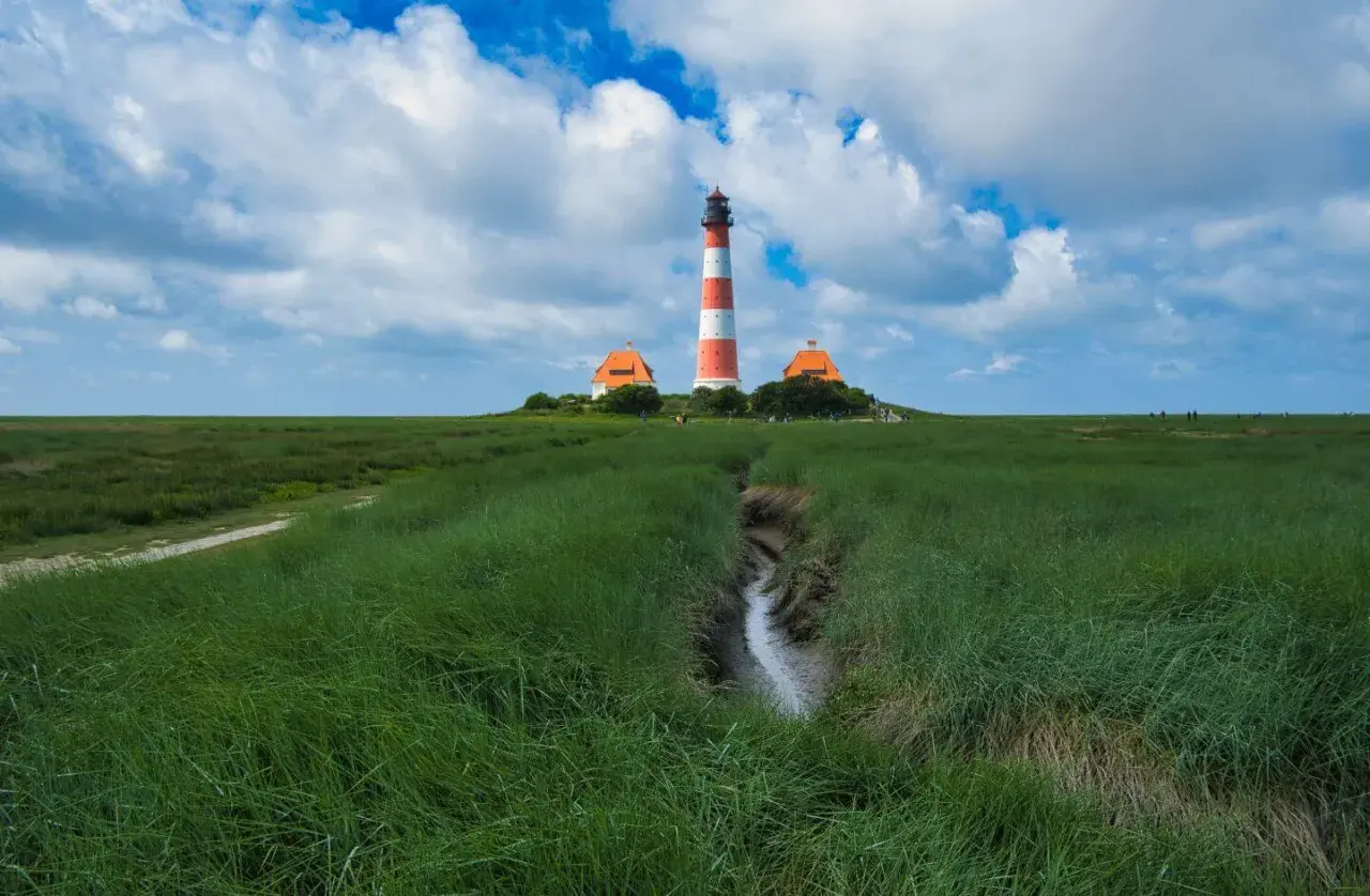 Leuchtturm Westerheversand, ein ikonischer fotospot in Schleswig-Holstein, ragt über grünes Marschland unter dramatischem Himmel.
