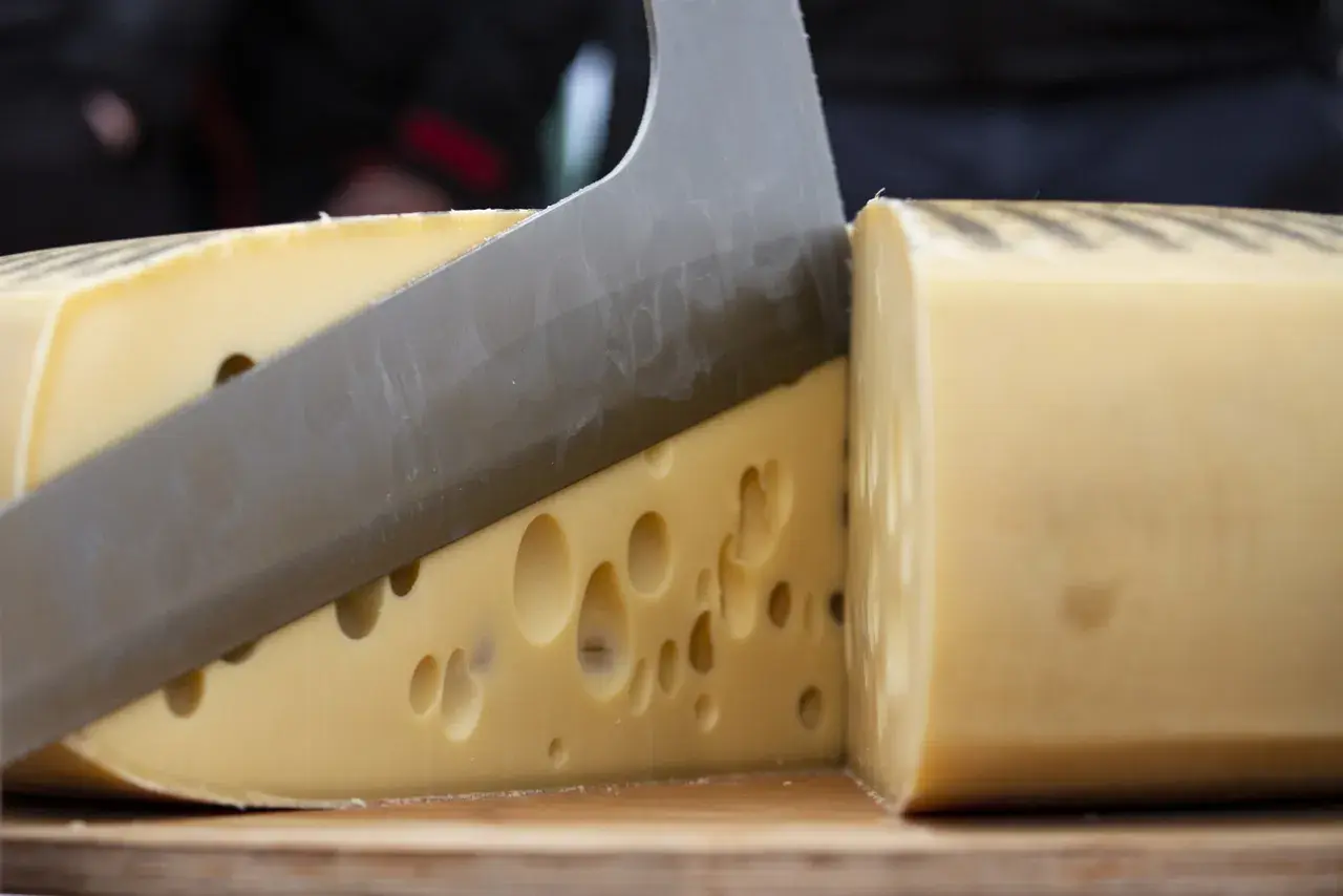 Un coltello affilato taglia un formaggio con i buchi, rivelando la sua consistenza invitante.