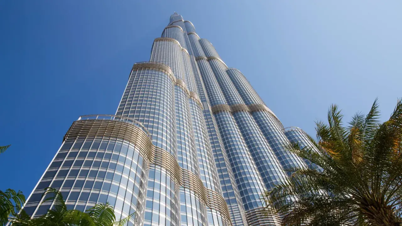 Burj Khalifa, najwyższy budynek na świecie, wznosi się ku błękitnemu niebu, otoczony palmami.