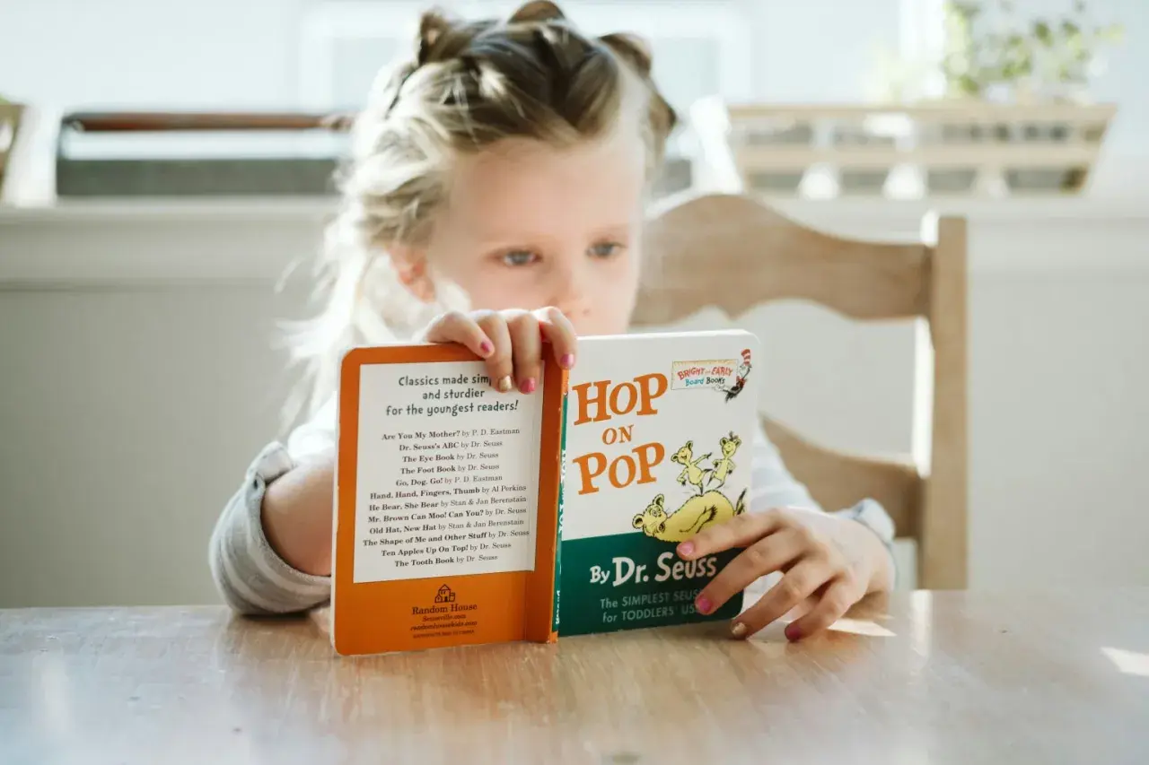 Dziewczynka czyta książki do czytania po angielsku, w tym "Hop on Pop" Dr. Seussa.