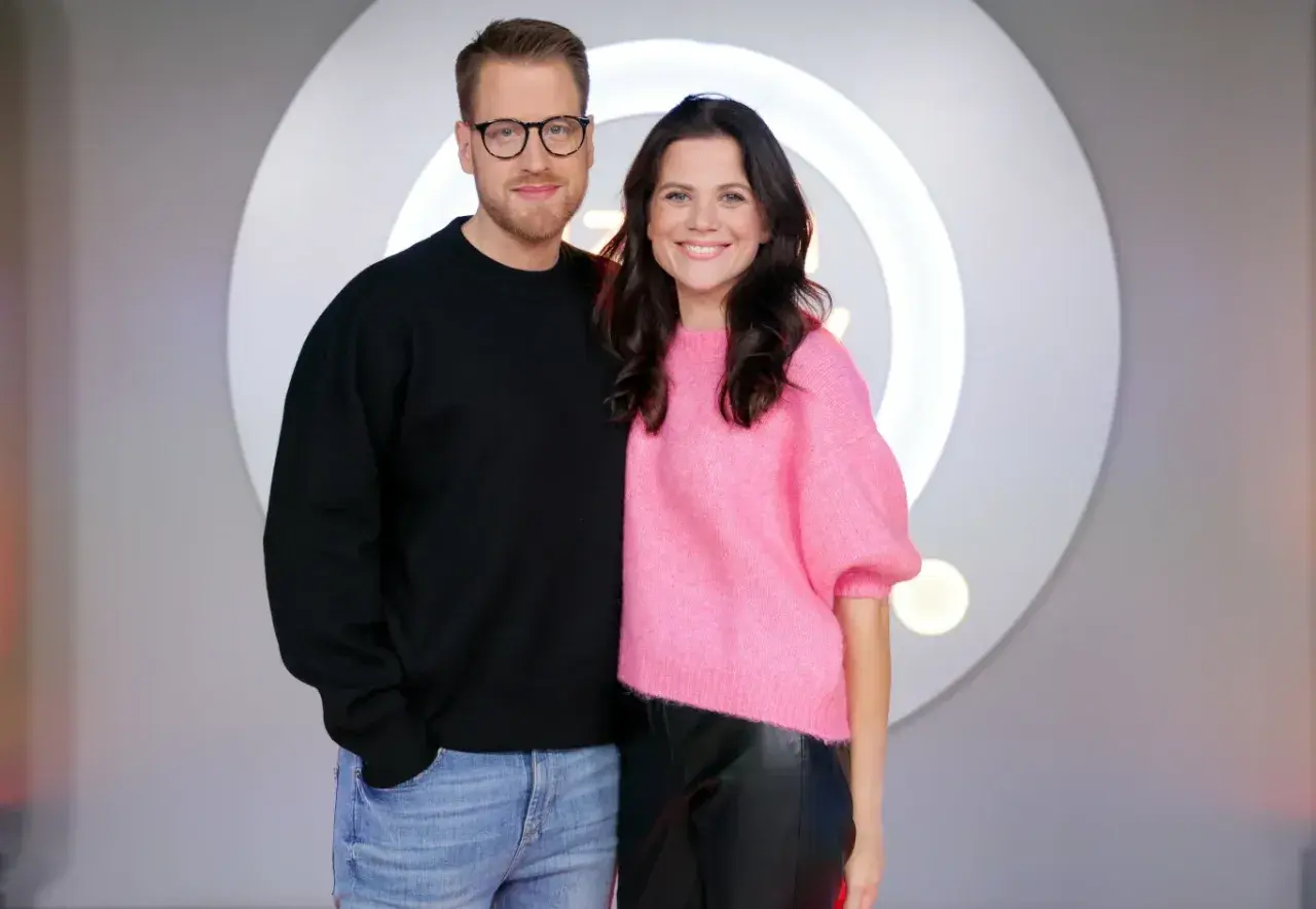 Patrycja Stockinger, dziennikarka, uśmiecha się obok kolegi w studiu telewizyjnym.