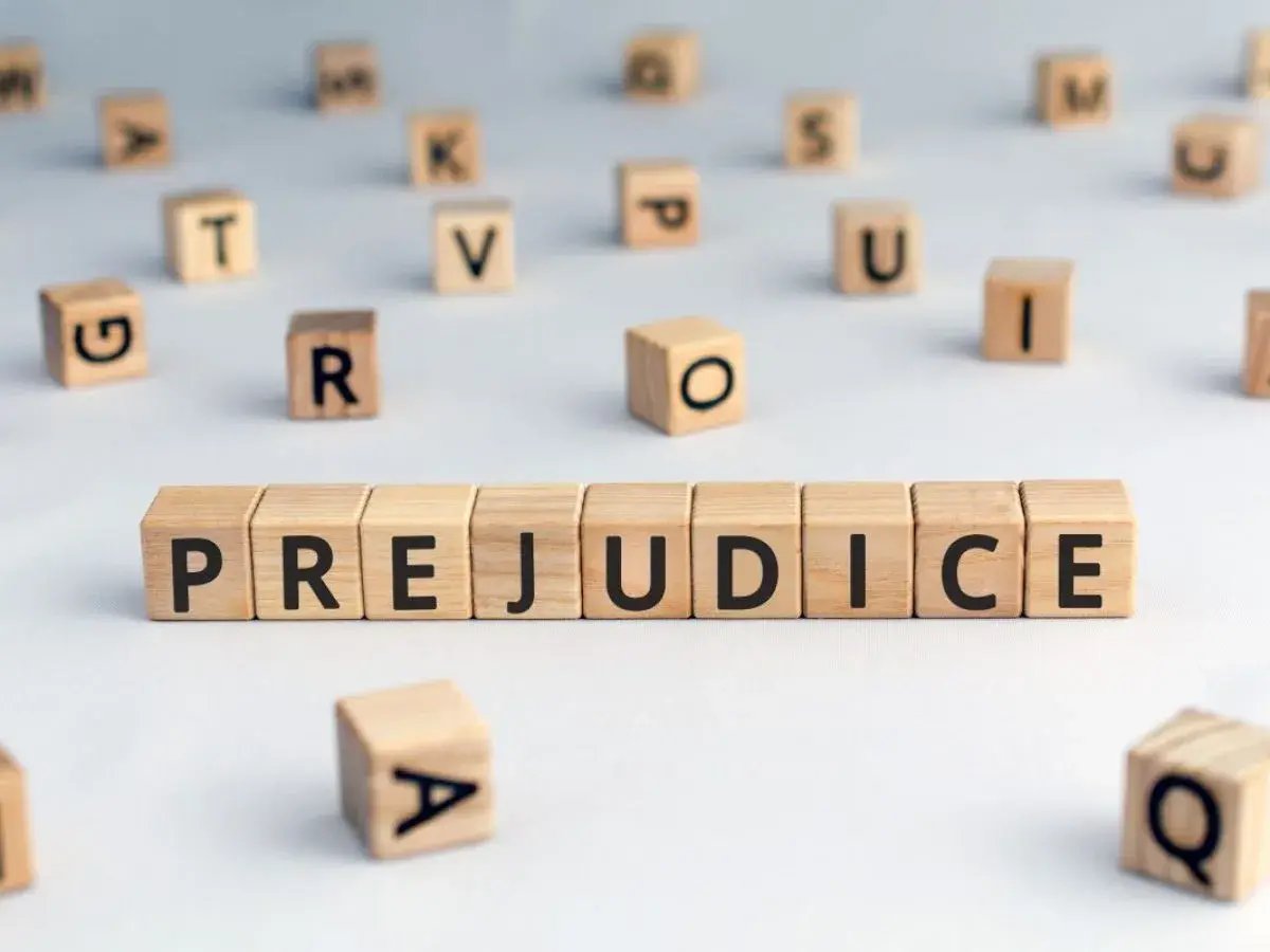 Des cubes en bois forment le mot "PREJUDICE", symbolisant le préjudice moral psychologique. D'autres lettres flottent autour.