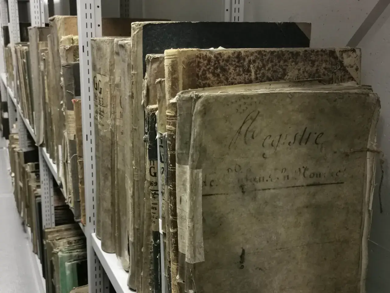 Des registres anciens, certains marqués "archive 07", s'alignent sur des étagères métalliques, témoins silencieux du temps.