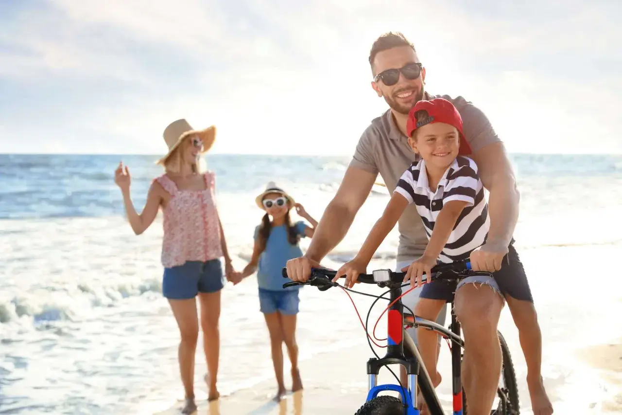 Famiglia felice in bicicletta sulla spiaggia, un'idea per le tue prossime idee viaggio con bambini in Italia.