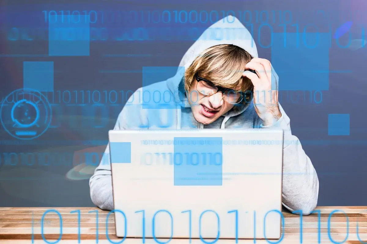Młody mężczyzna w kapturze zmagający się z problemem, zastanawia się, adware co to jest. Cyfrowy kod otacza go.