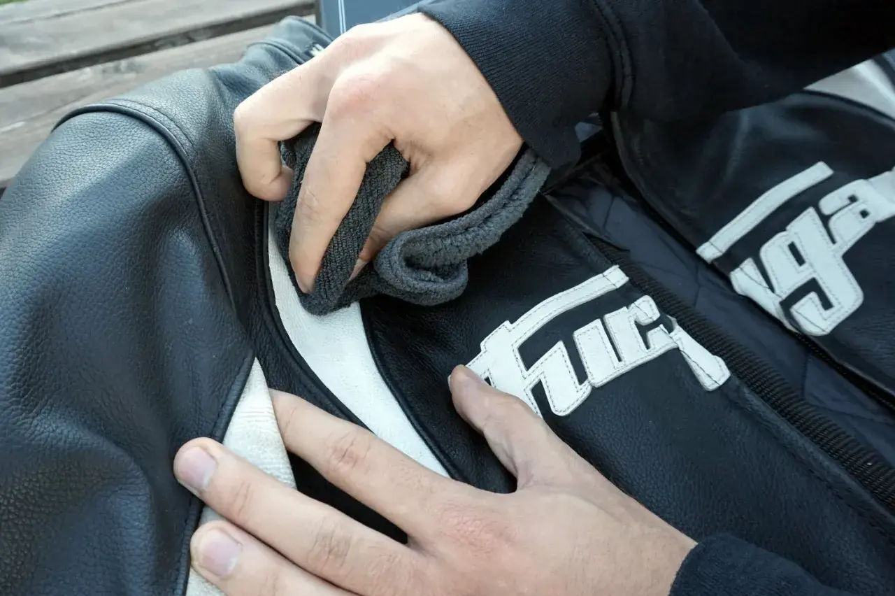 Manos limpian chaqueta de moto de cuero negro con detalles blancos. Aprende como lavar una chaqueta de moto.