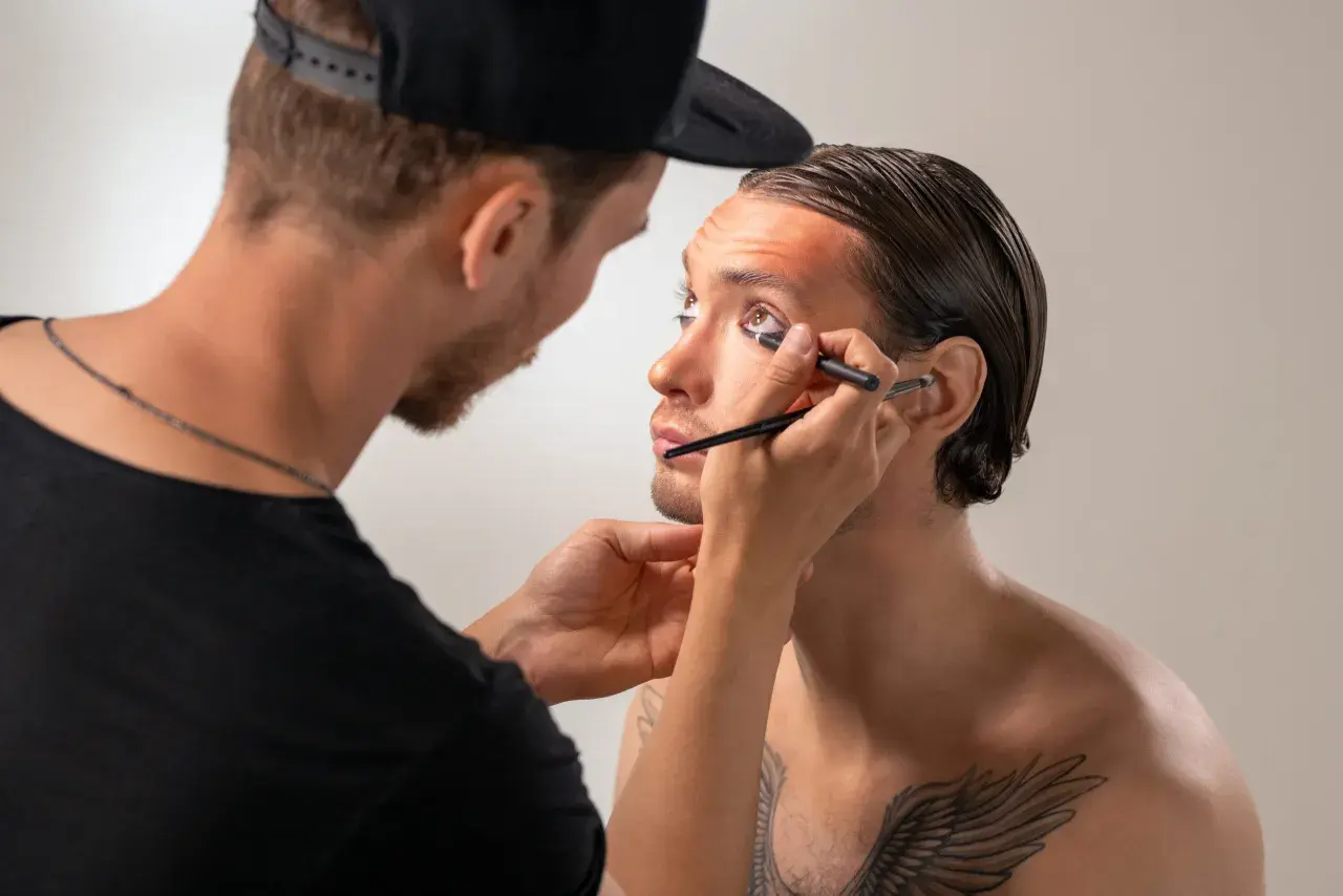 Un truccatore applica l'eyeliner a un modello, creando un look audace.