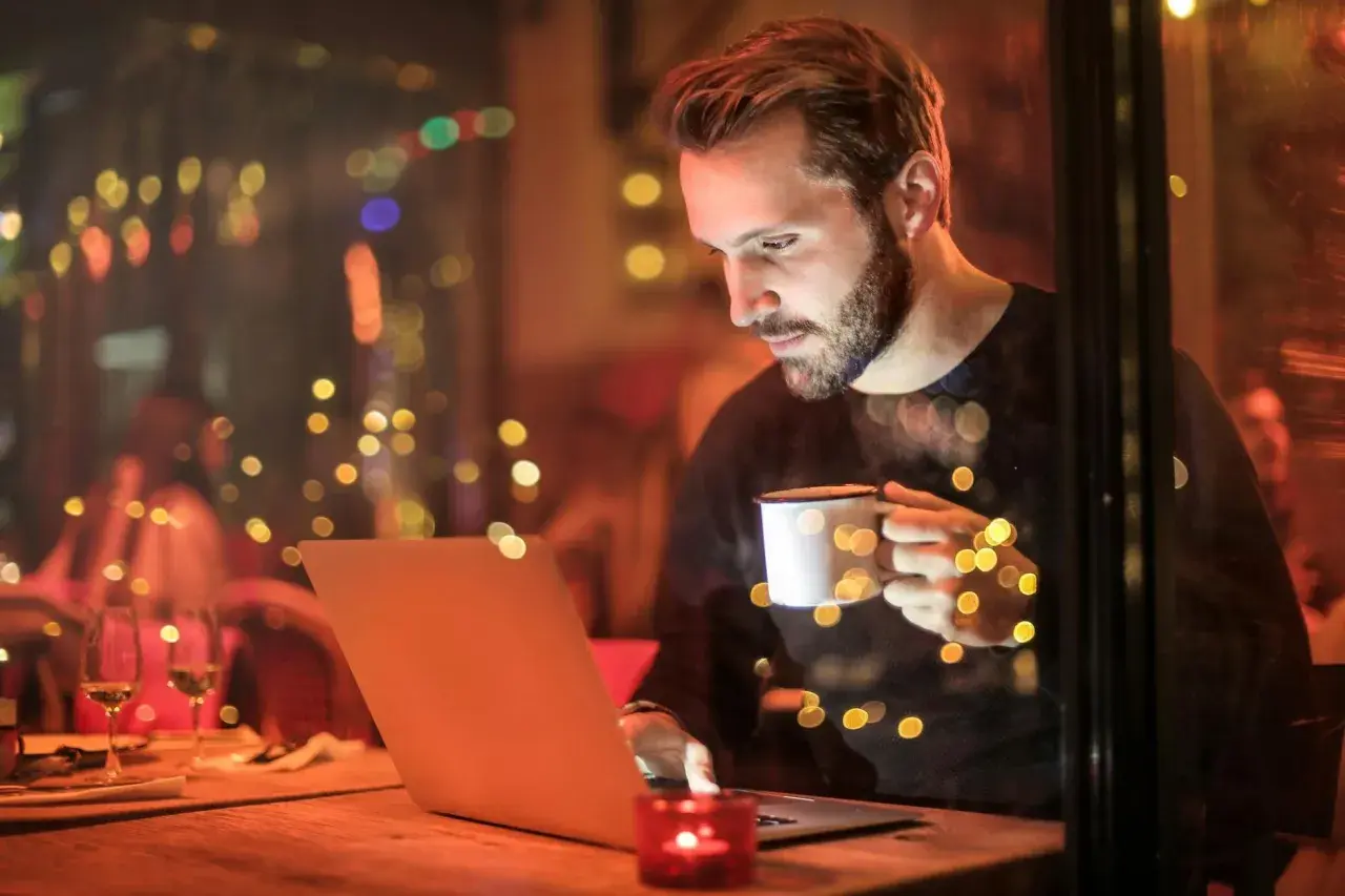 Mężczyzna z kubkiem kawy pracuje na laptopie, szukając informacji o tym, jaki internet do domu bez światłowodu będzie najlepszy.