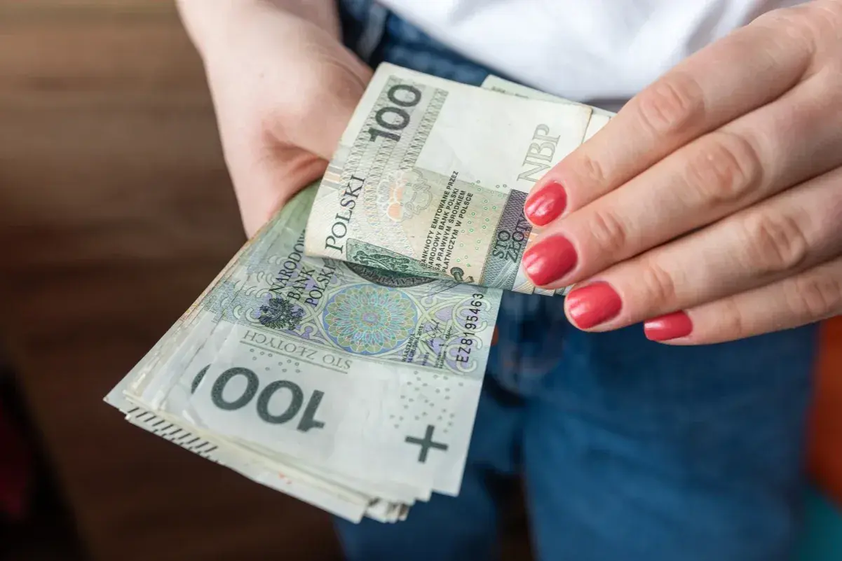 Dłonie z czerwonymi paznokciami trzymają stos banknotów 100 zł. To polska stopa referencyjna NBP.