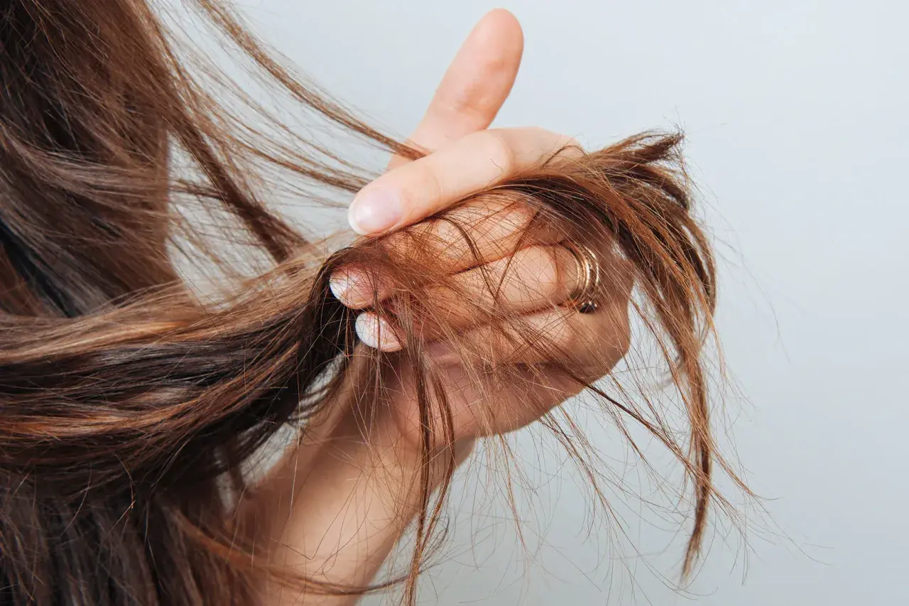Mano che mostra capelli con doppie punte, un segno di capelli secchi e danneggiati che necessitano di cure.