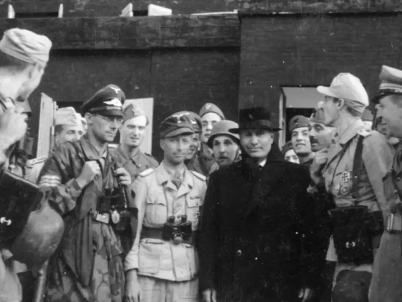 Grupp av män, varav en med hatt och rock, möjligen Otto Skorzeny, omgiven av militärer i uniform.