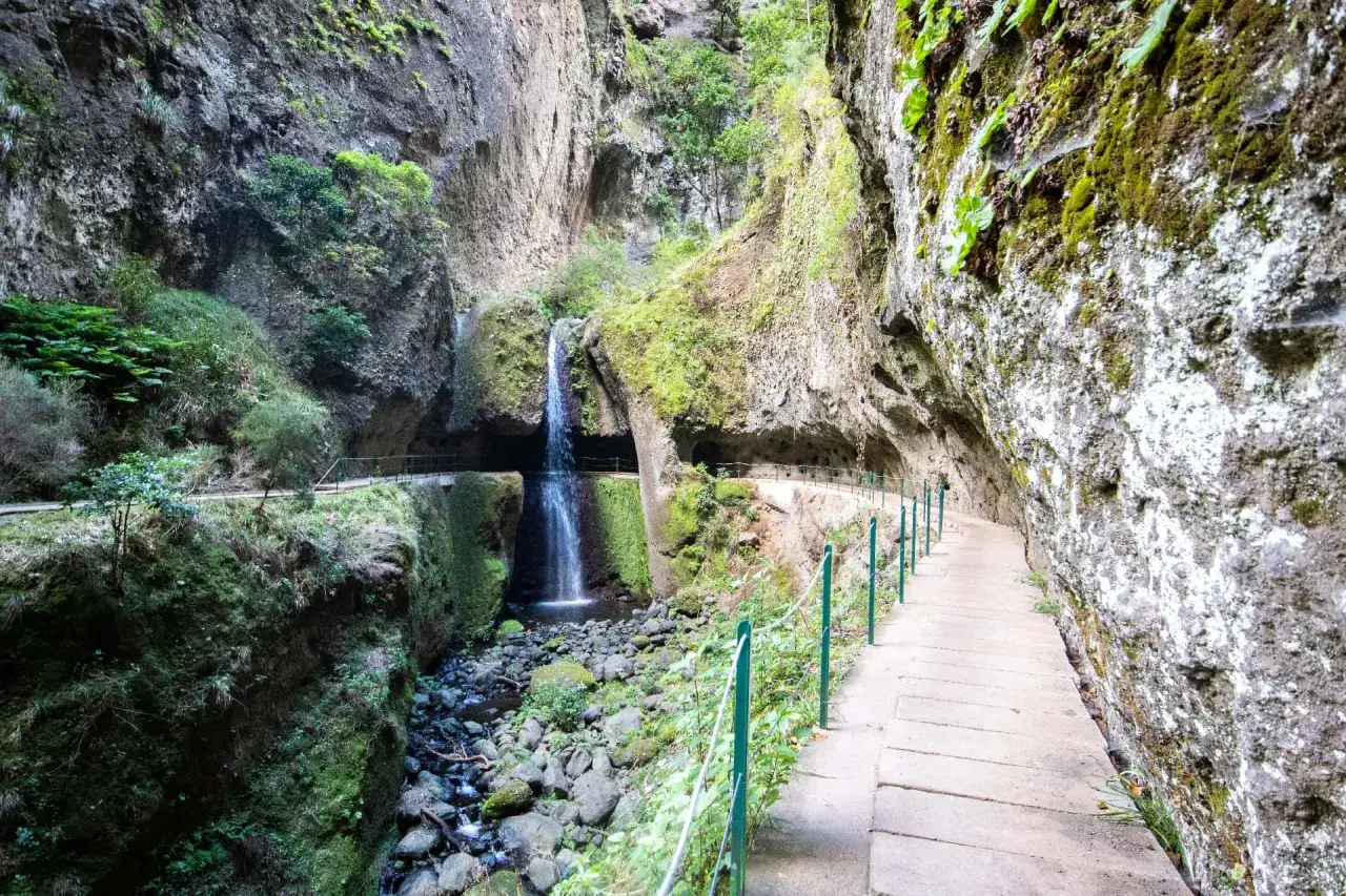 A scenic path along the Levada do Moinho leads to a cascading waterfall nestled within a moss-covered canyon.