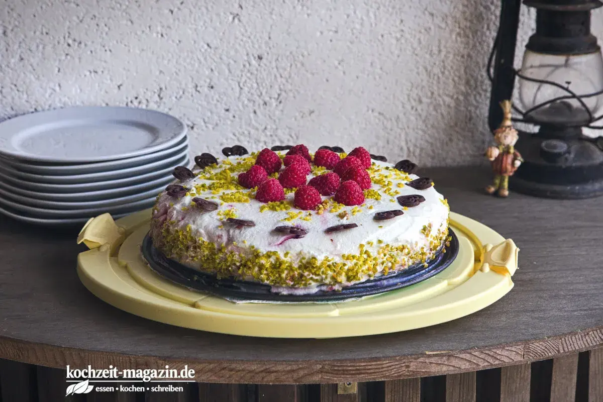 Himbeer Joghurt Torte mit frischen Beeren und Pistazien, verziert mit Schokoladenherzen. Ein Genuss für jeden Anlass.