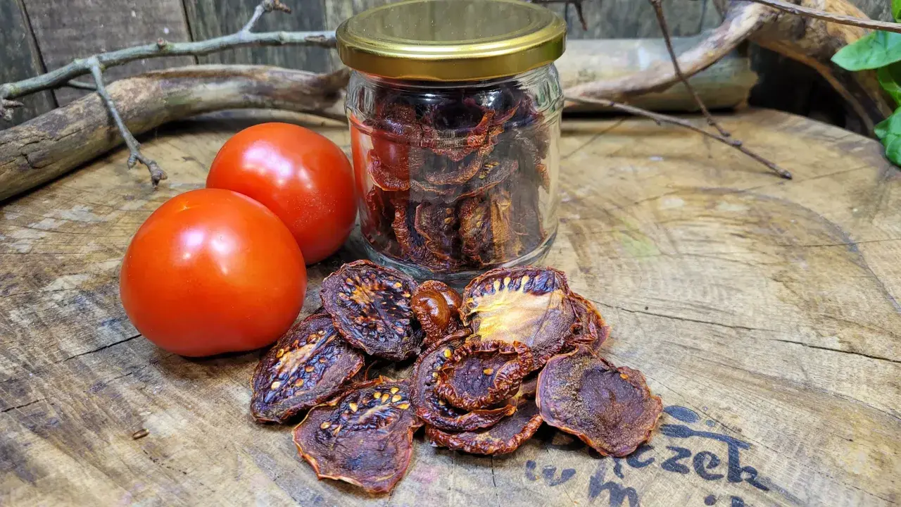 Słoik pełen aromatycznych suszonych pomidorów obok świeżych pomidorów i gałązek na drewnianym blacie.