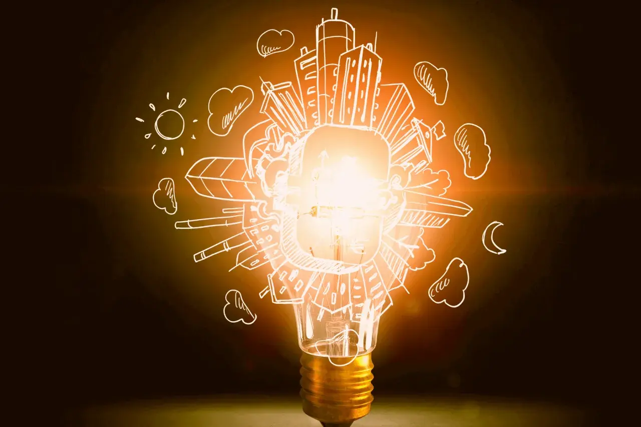 Bombilla encendida con dibujos de ciudad, sol y luna. Representa la diferencia entre potencia y energía, la chispa de una idea.