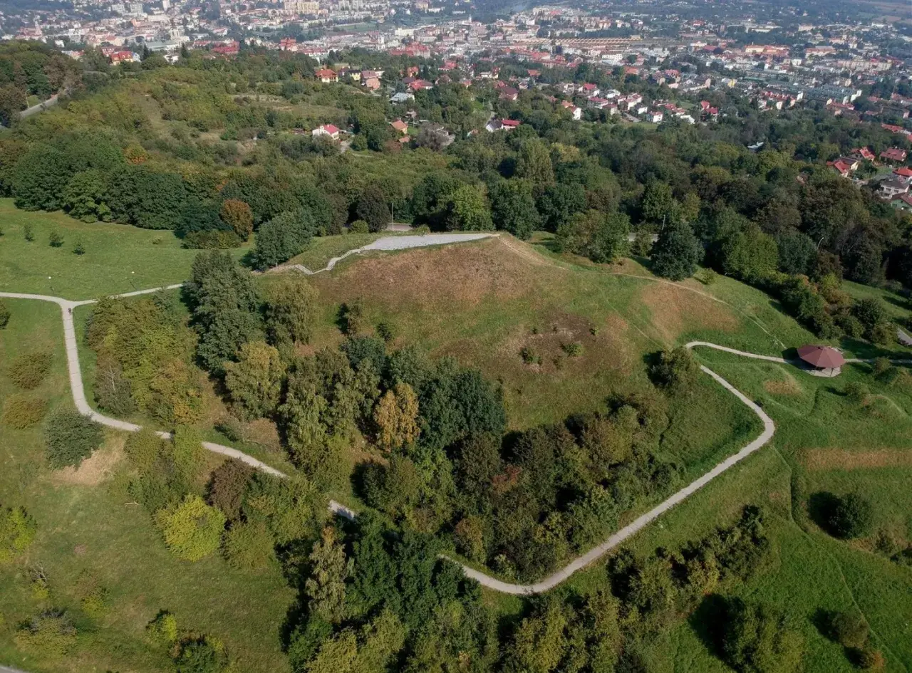 Widok z lotu ptaka na Kopiec Tatarski w Przemyślu, otoczony zielenią i wijącymi się ścieżkami. W oddali widać panoramę miasta.