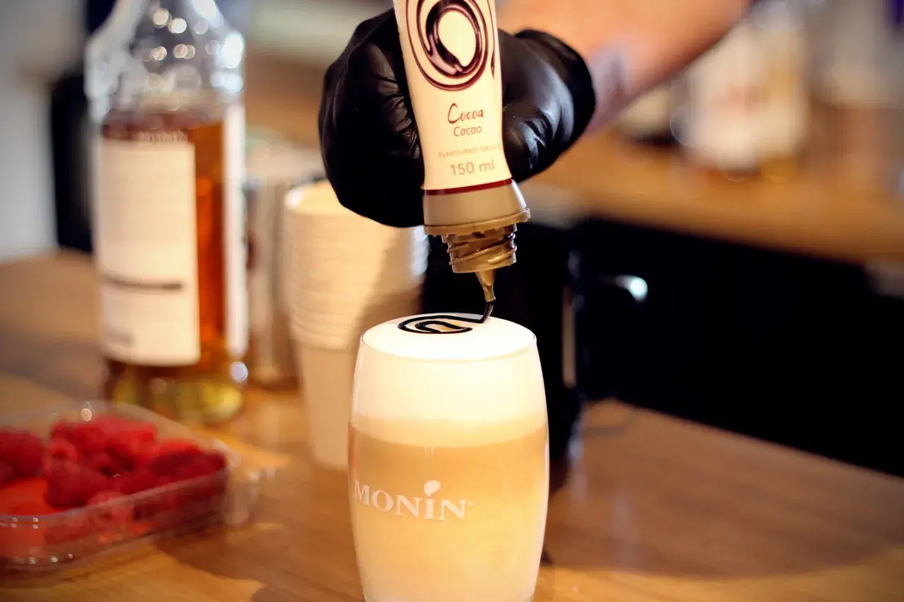 Barista ozdabia gorącą czekoladę do picia syropem kakaowym.