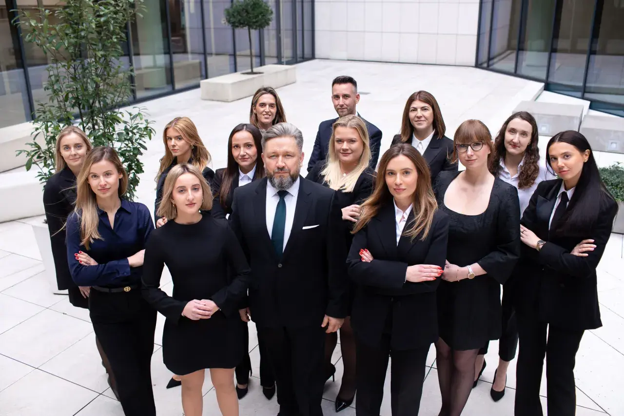 Grupa prawników w garniturach i sukienkach stoi przed nowoczesnym budynkiem.