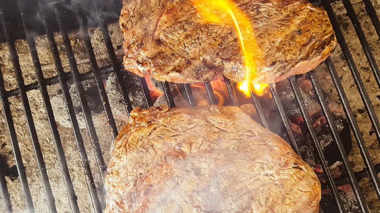Två saftiga biffar grillas med ved. Flammor slickar köttet som får en perfekt yta.