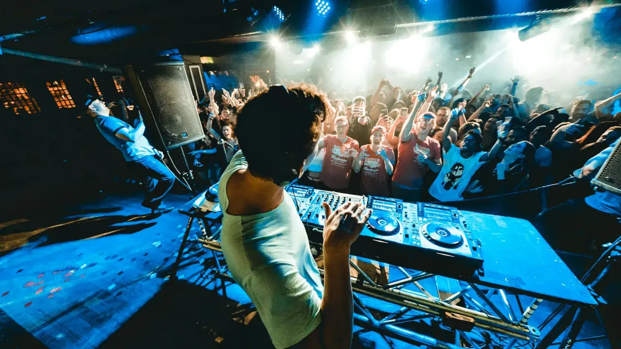 DJ na scenie, tłum szaleje w rytm drum and bass. Niebieskie światła, dym i energia.
