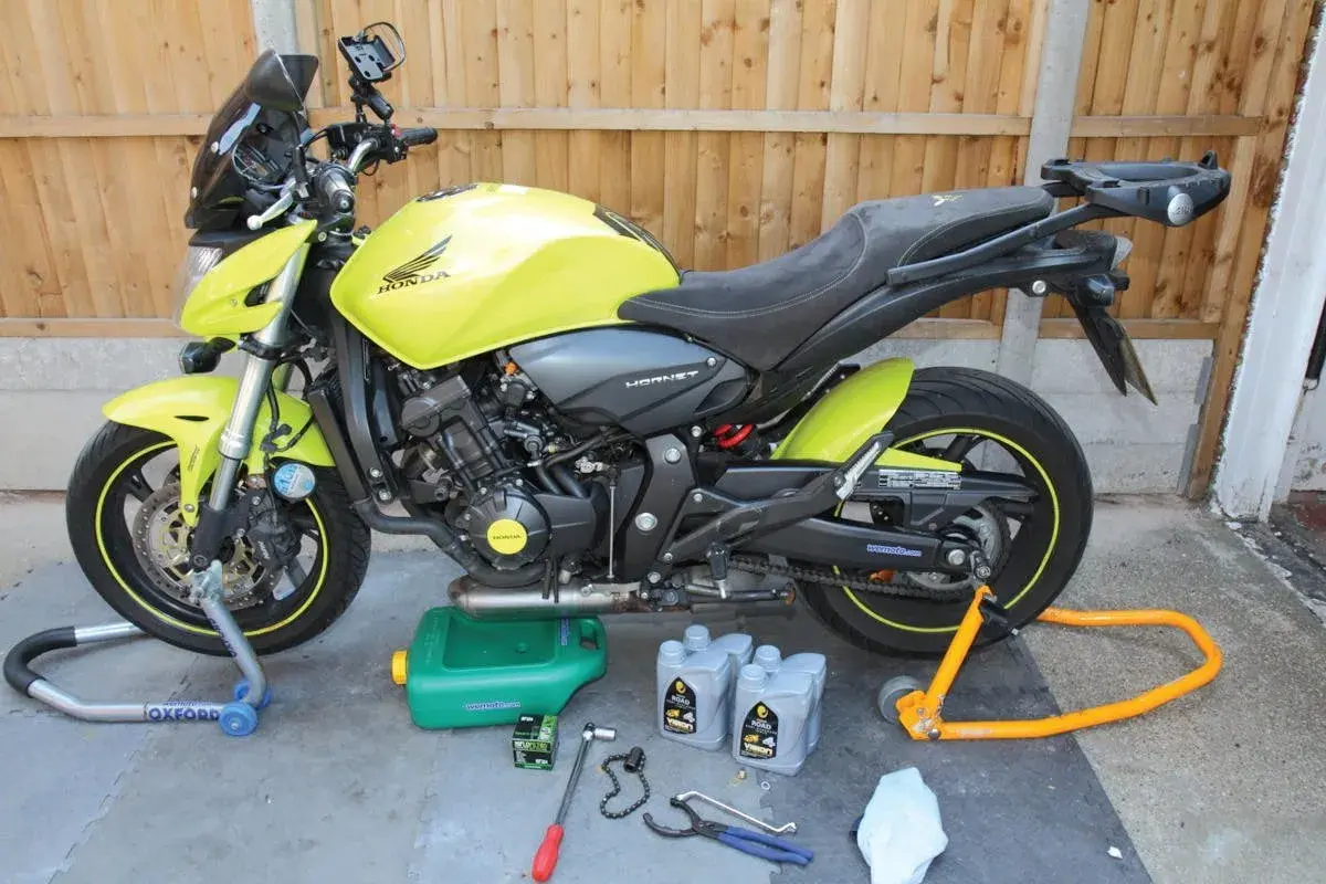 Moto Honda Hornet gialla pronta per cambiare l'olio di lubrificazione del motore. Attrezzi e olio a terra.
