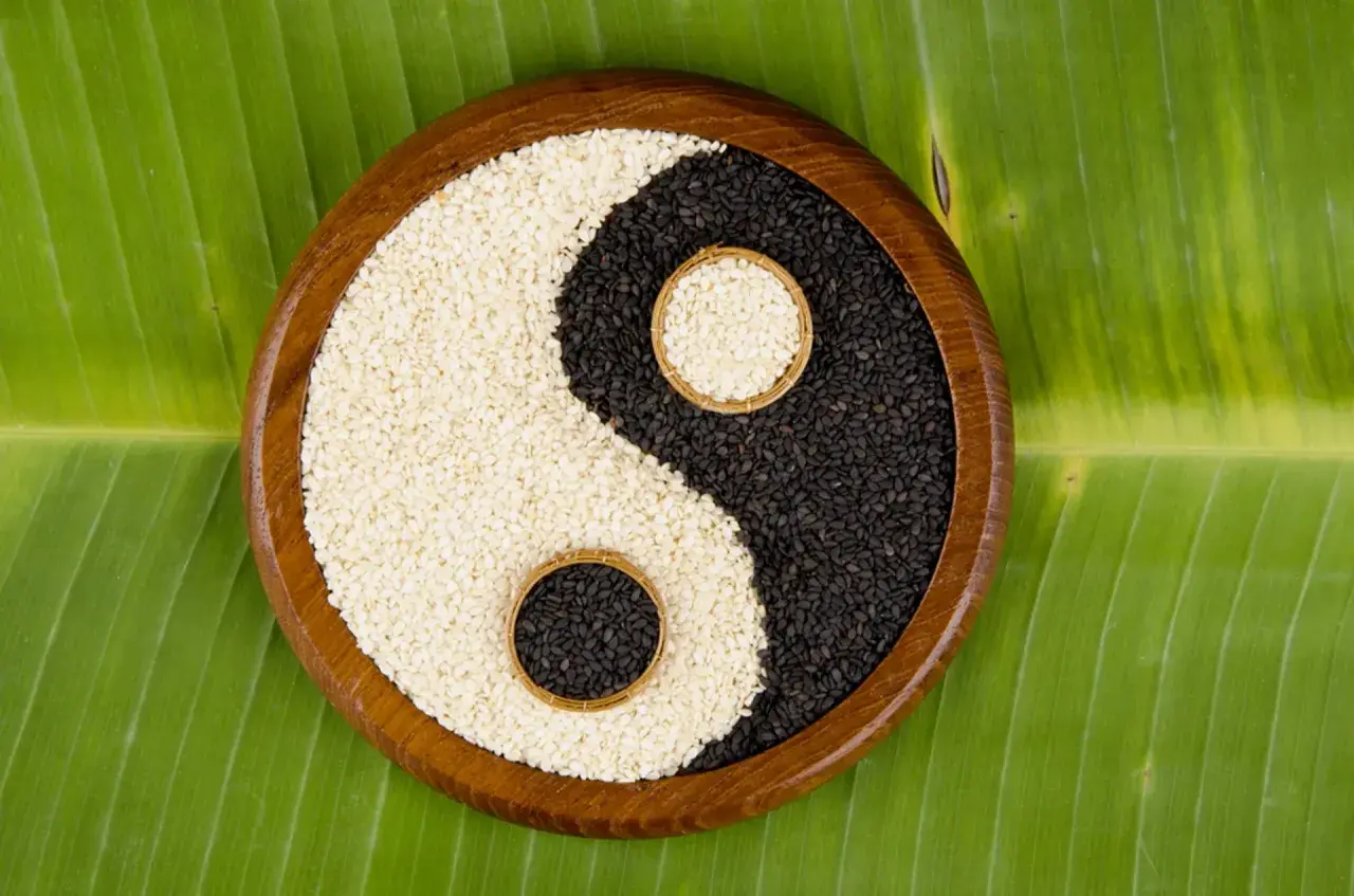 Simboli yin e yang di semi di sesamo bianchi e neri, disposti su una foglia verde.