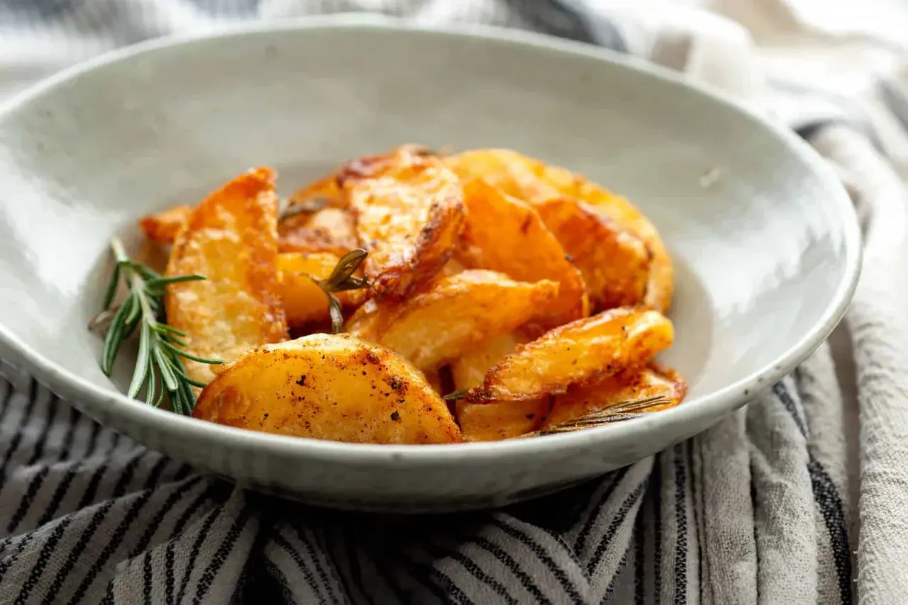 Patatas al horno en rodajas, doradas y crujientes, servidas en un cuenco con romero fresco.