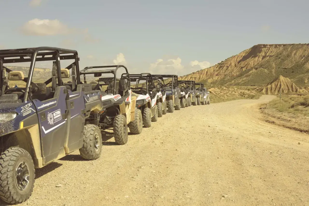Una fila de vehículos todoterreno espera en un camino de tierra, listos para una aventura por el desierto, como si fueran un puente de todos los santos hacia lo desconocido.