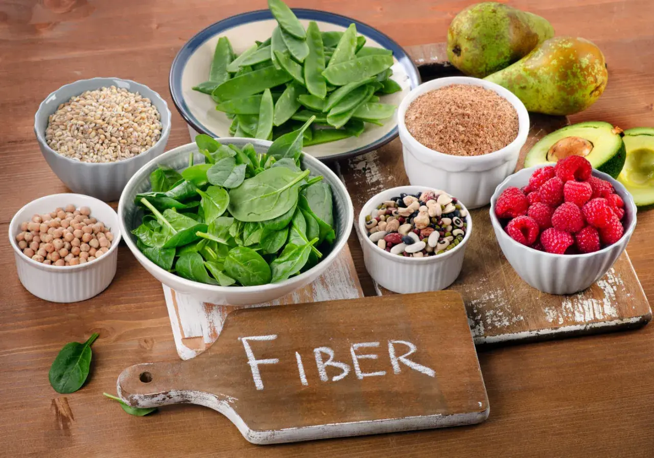 En skärbräda med texten "FIBER" omgiven av skålar med bönor, linser, spenat, hallon, päron, avokado och korn.