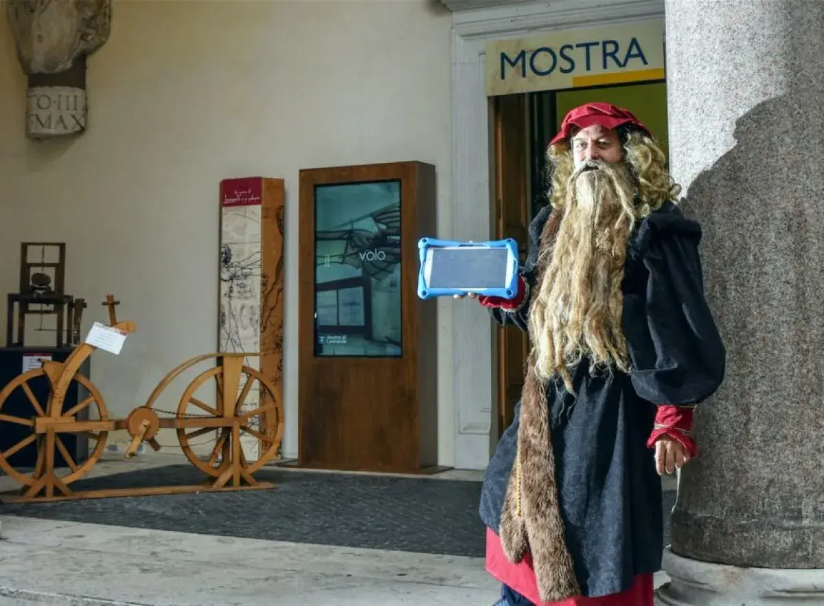 Uomo vestito da Leonardo da Vinci con tablet, pronto per una caccia al tesoro a Roma, vicino a un'antica bicicletta di legno.