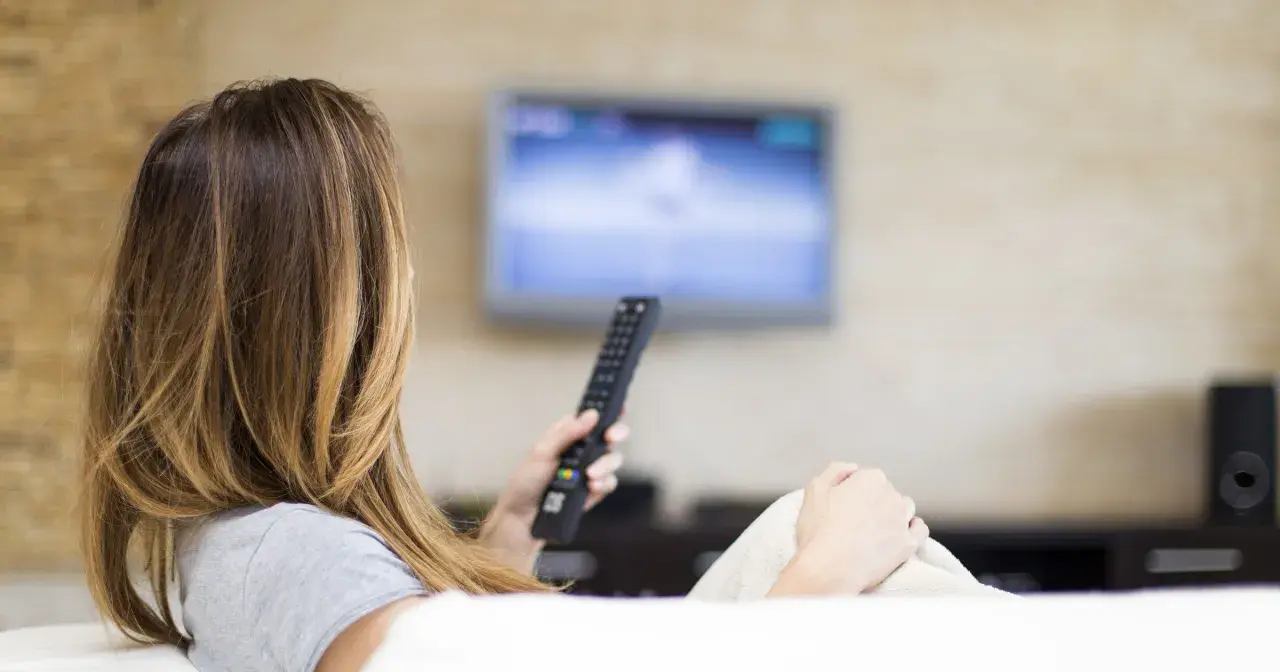 Kobieta z pilotem w ręku ogląda telewizję, ciesząc się swoim abonamentem radiowo-telewizyjnym.