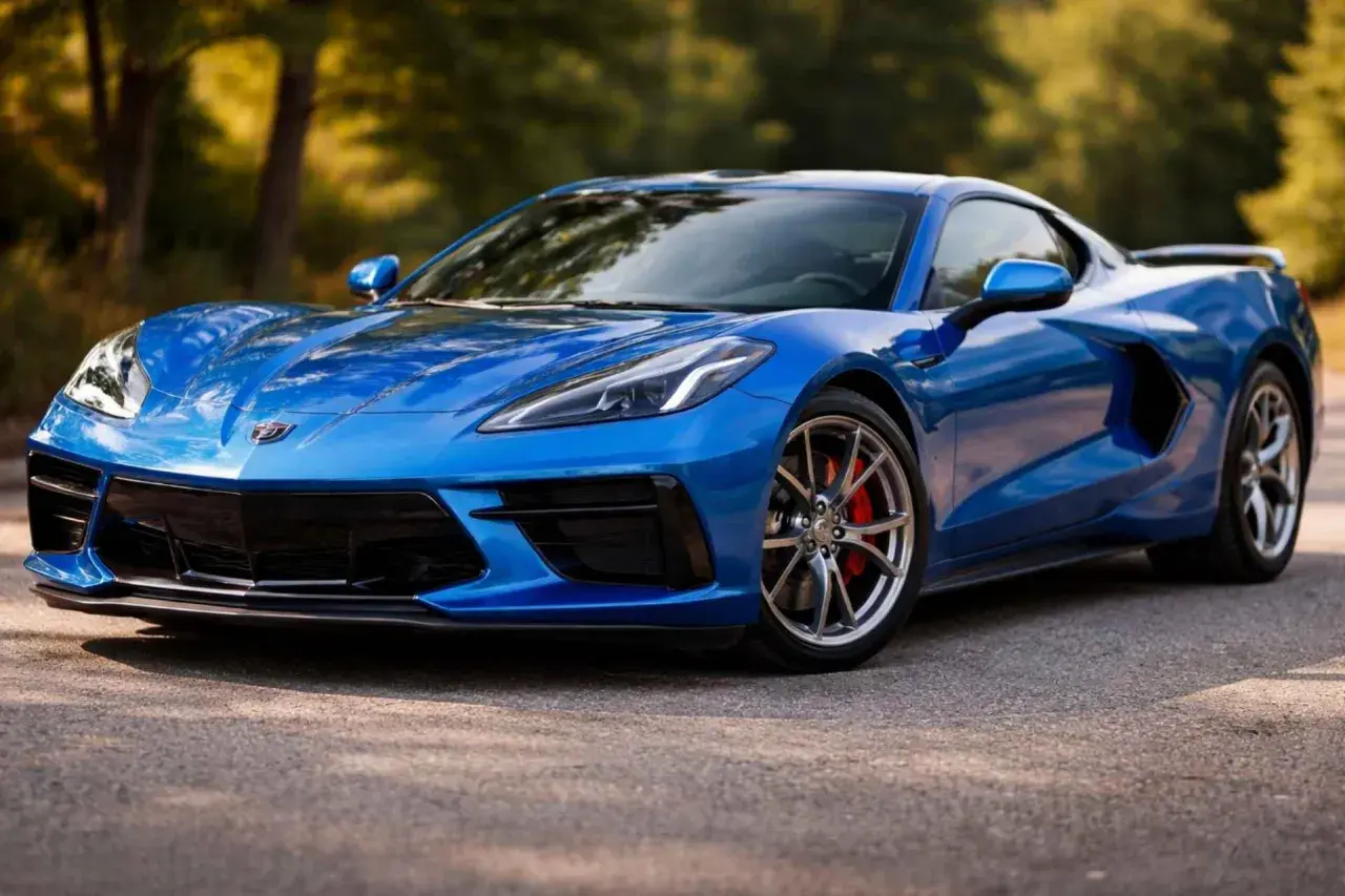 Błękitny Chevrolet Corvette Stingray z czerwonymi zaciskami hamulcowymi na tle drzew.