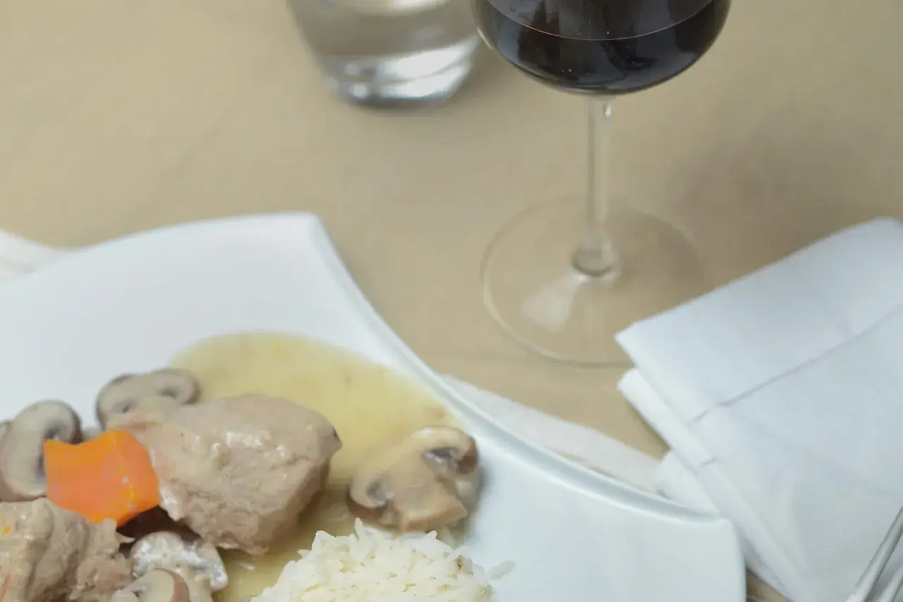 Un verre de vin rouge accompagne une blanquette de veau savoureuse avec riz et champignons.