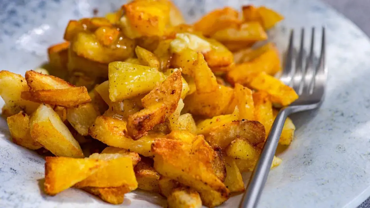 Un plato de papas al horno crujientes, doradas y sazonadas, listas para disfrutar con un tenedor.