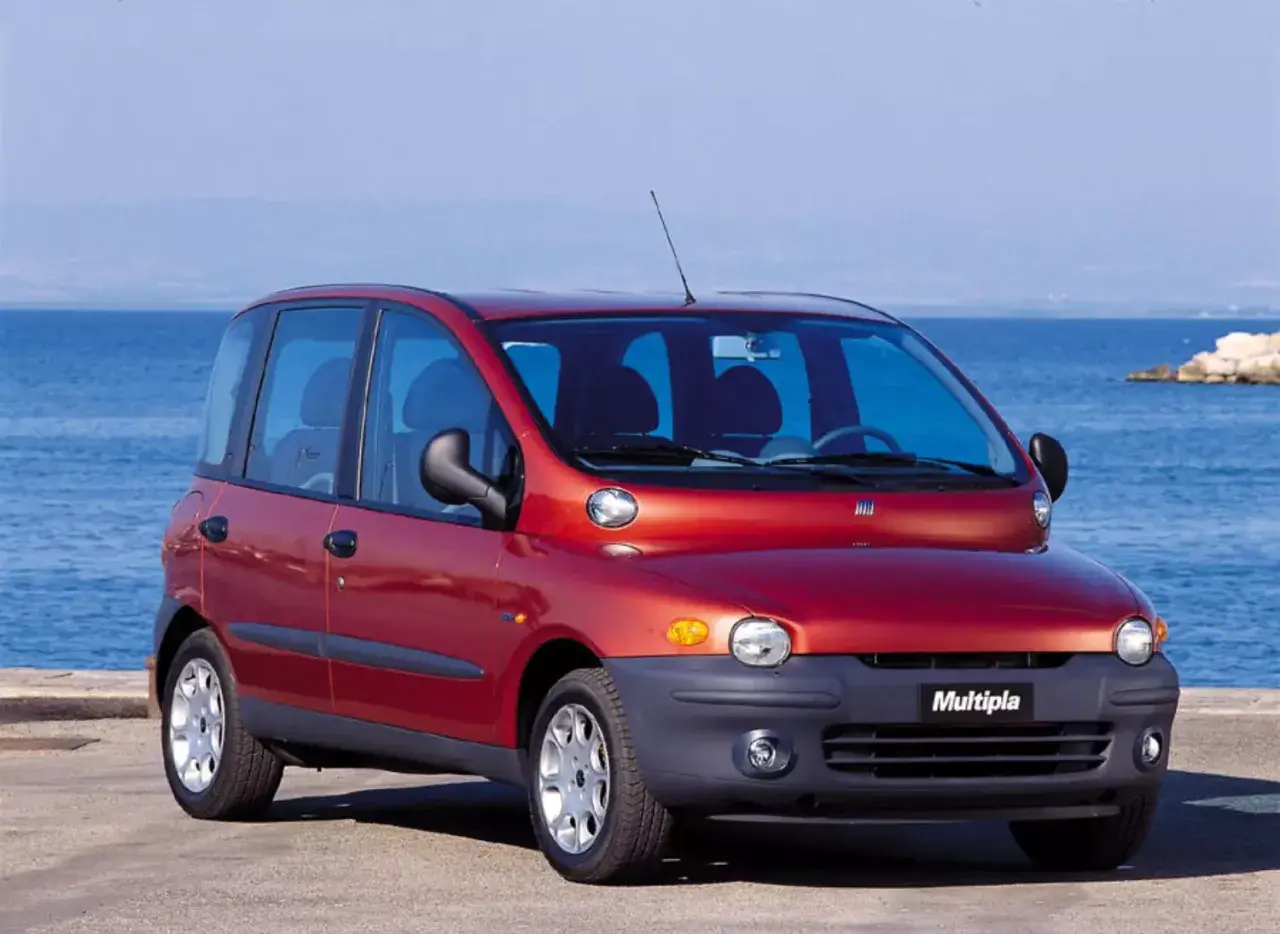 Czerwony Fiat Multipla, często uznawany za najbrzydsze auto na świecie, stoi nad morzem.