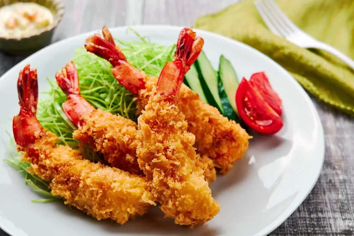 Crispy, golden japanese fried shrimp served on a bed of shredded cabbage with cucumber and tomato slices.