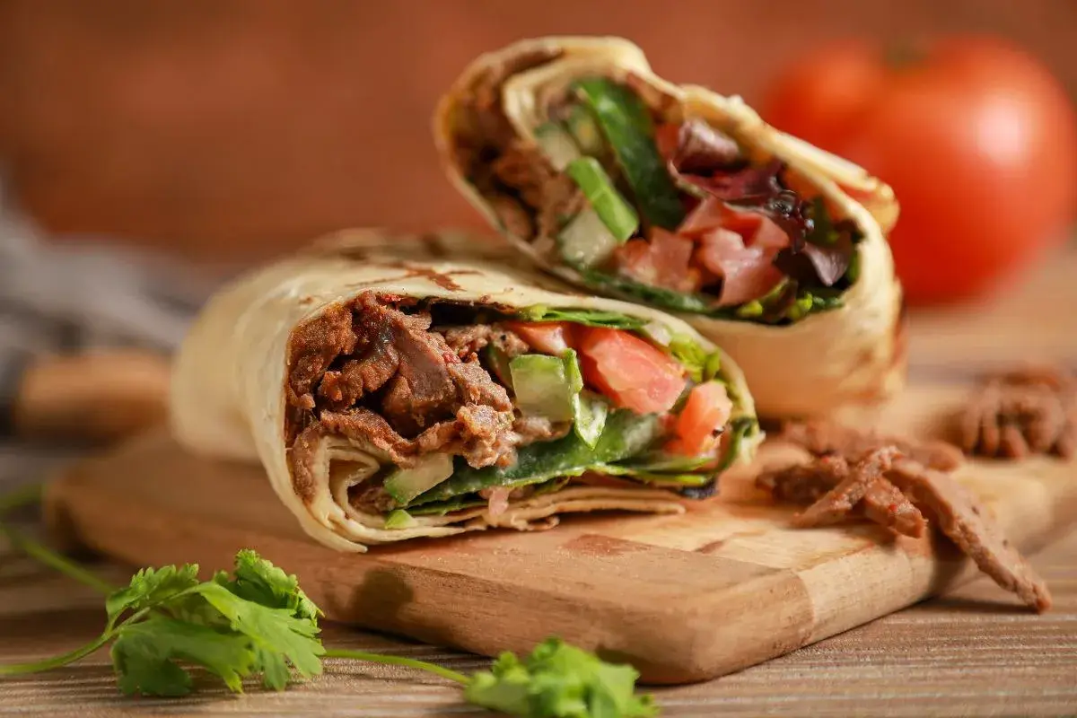 Kebab zawinięty w tortillę z mięsem, warzywami i ziołami na desce.