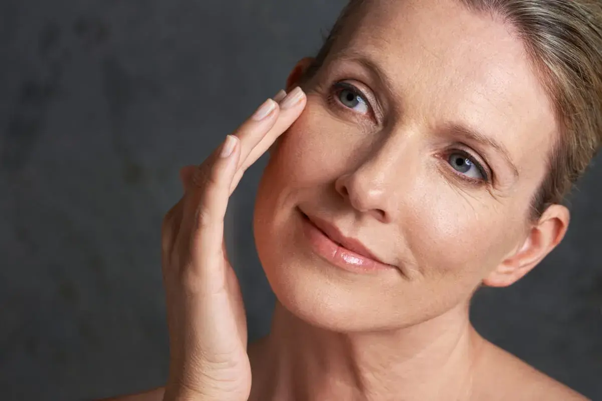 Une femme touche délicatement son visage, révélant une peau mature. La question "peau mature à partir de quel âge" se pose naturellement.