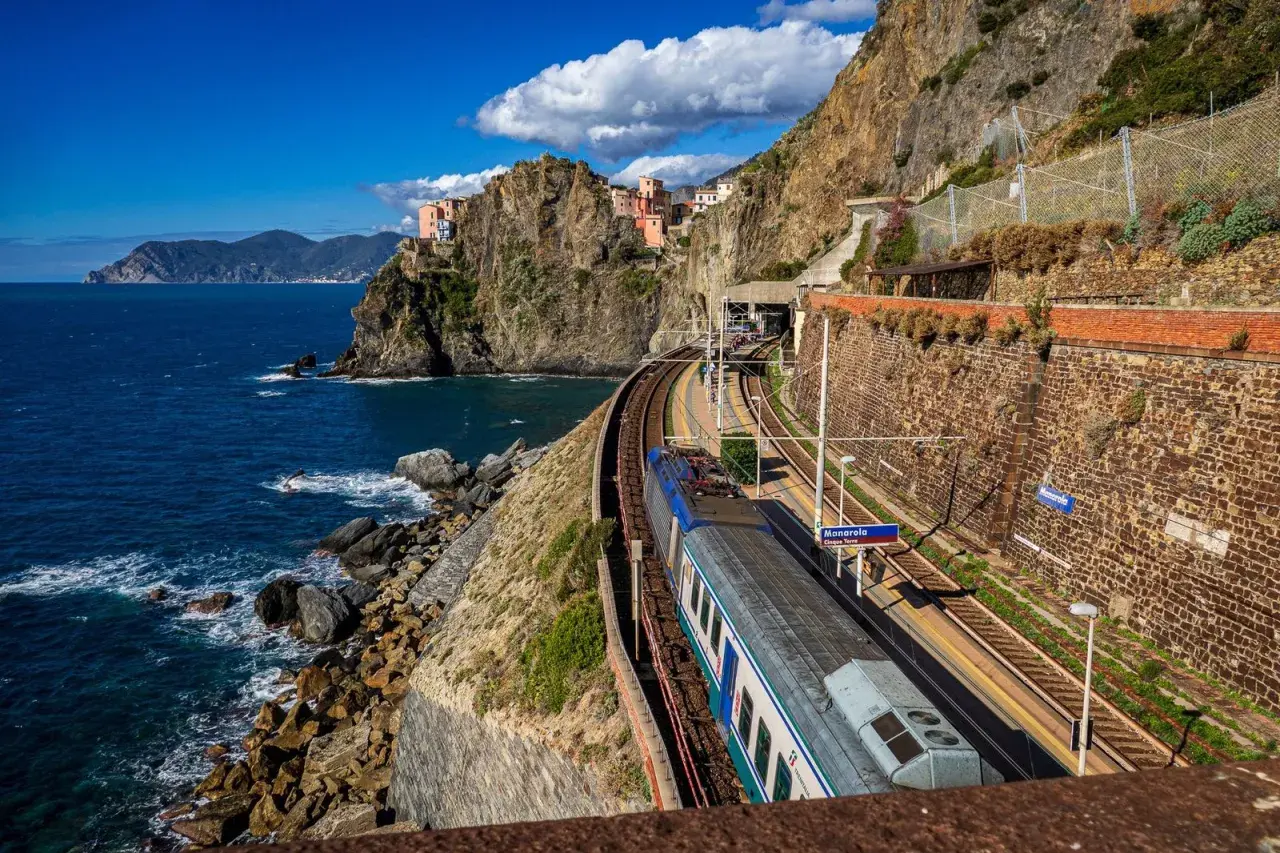 Zug fährt entlang der Küste von Cinque Terre. Bunte Häuser kleben an steilen Felsen über dem blauen Meer.