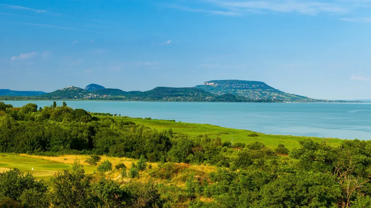 Malowniczy krajobraz z jeziorem Balaton na Węgrzech, zielone wzgórza i błękitne niebo.