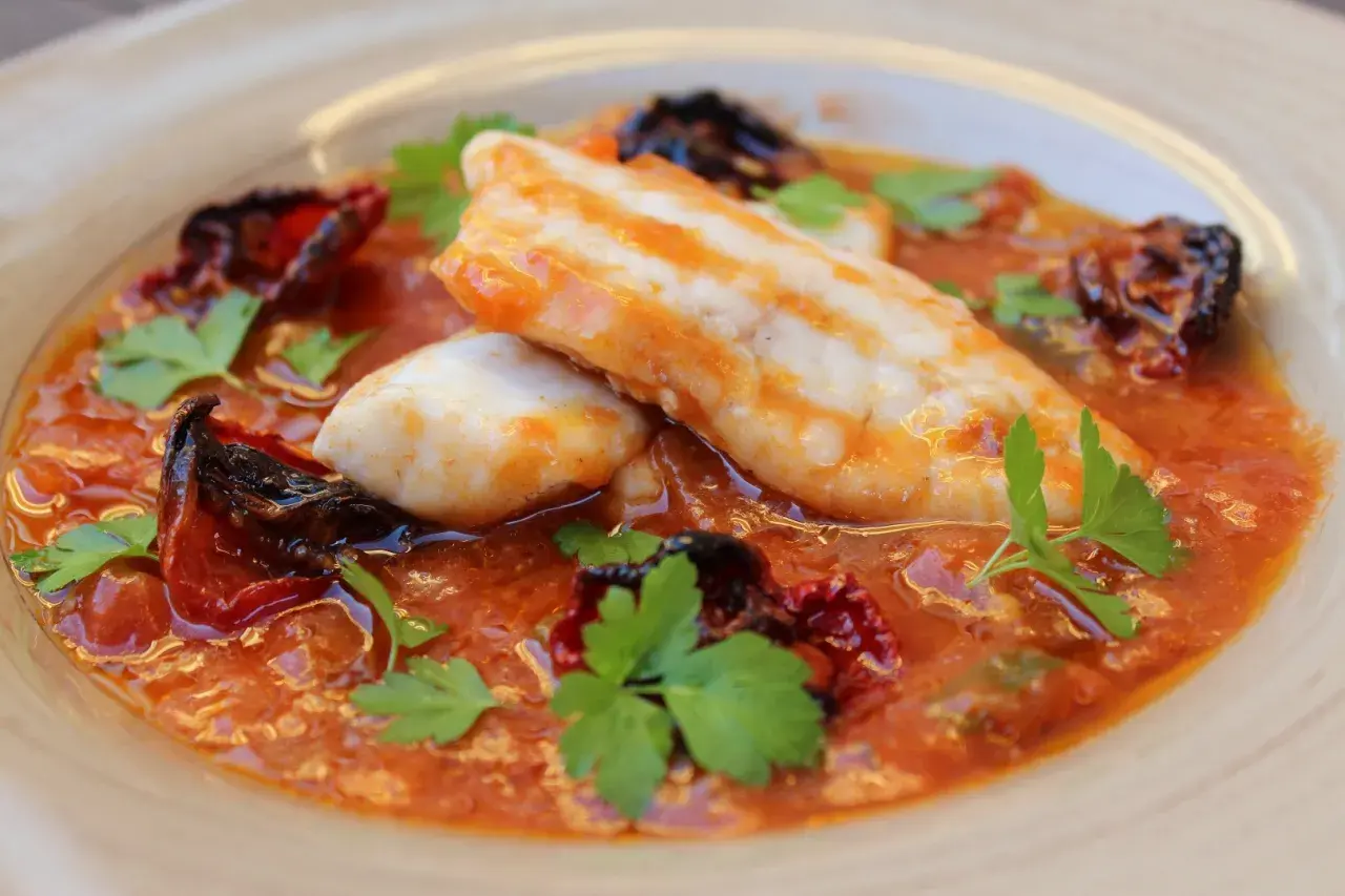 Deliciosa ventresca de merluza en salsa de tomate con pimientos secos y perejil fresco.