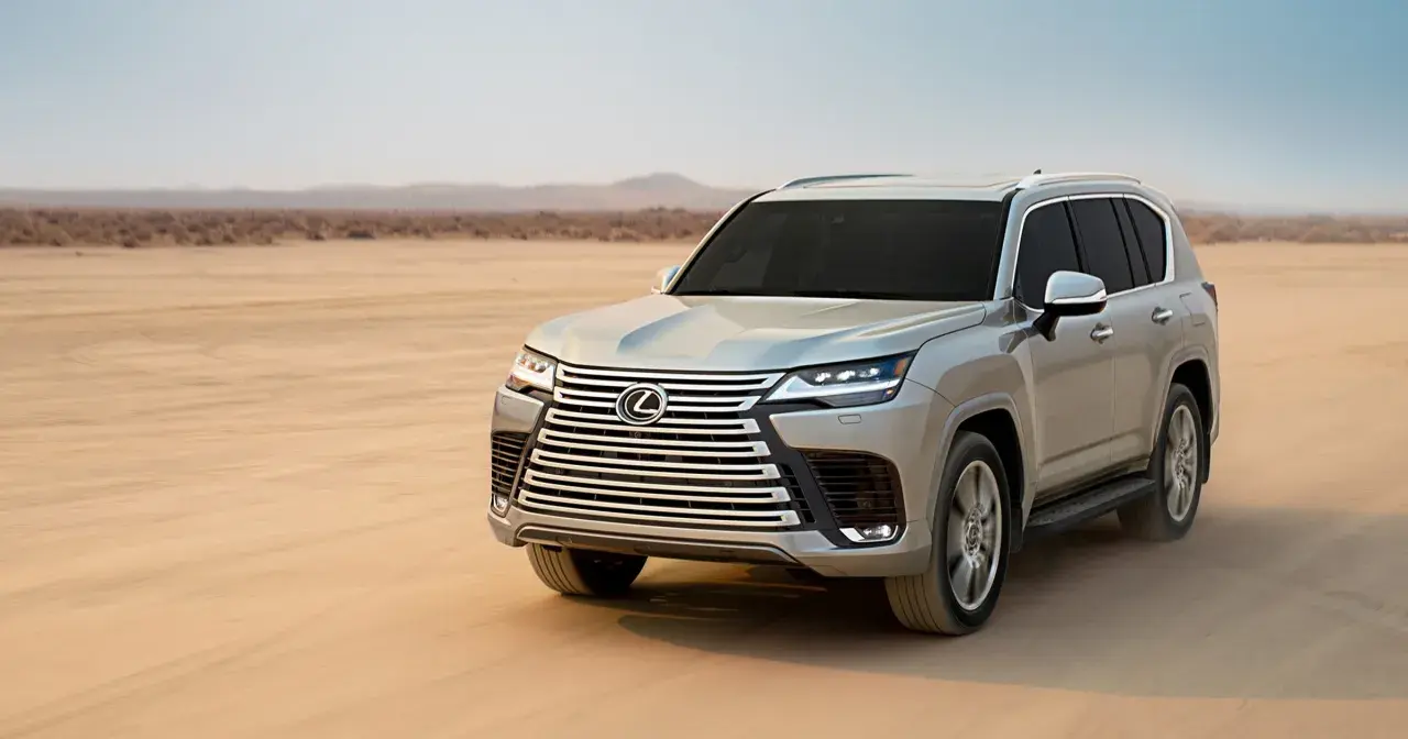 Srebrny Lexus LX 600 przemierza pustynię, unosząc tumany piasku.