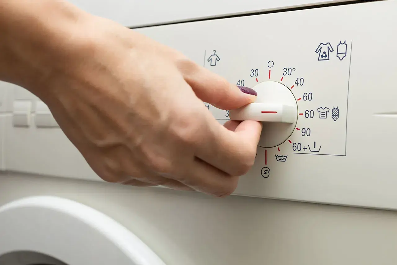 Main d'une personne réglant le bouton d'une machine à laver pour le lavage de vêtements.