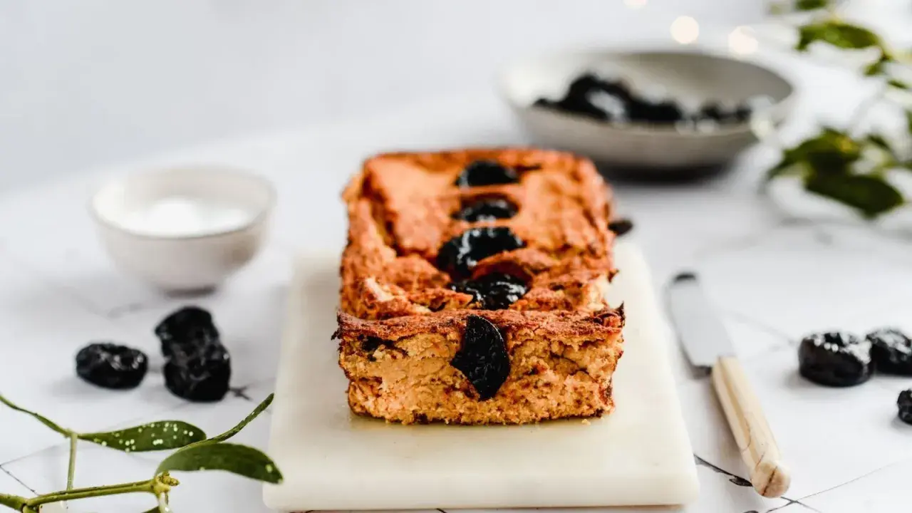 Domowy pasztet z resztek mięsa pieczonego, ozdobiony śliwkami, na desce z nożem i miseczką sosu.