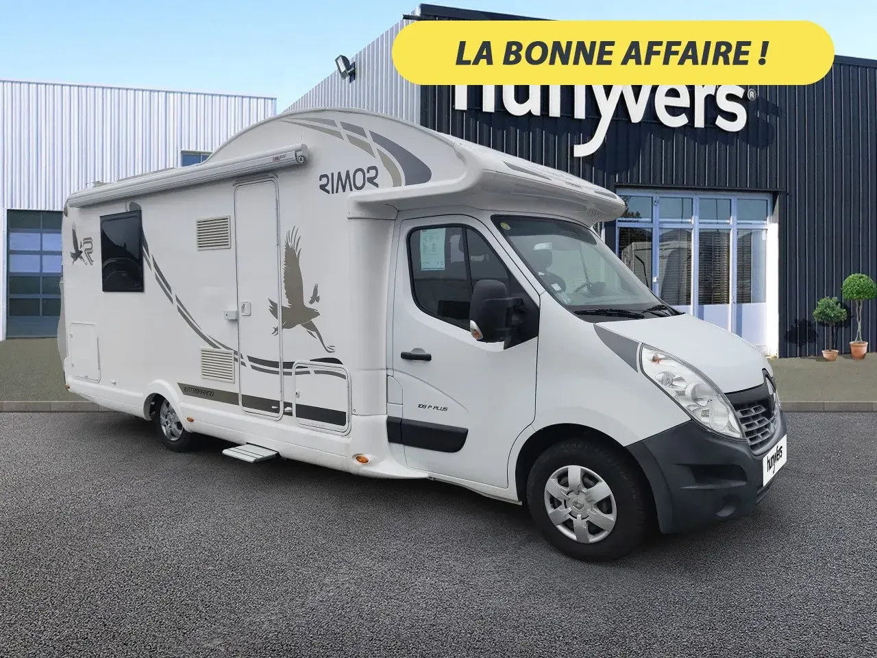 Un camping-car Rimor Katamarano 109 Plus blanc, avec un aigle stylisé sur le flanc, prêt pour l'aventure.