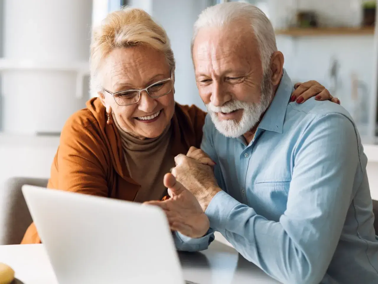 Uśmiechnięta para seniorów korzystająca z laptopa.