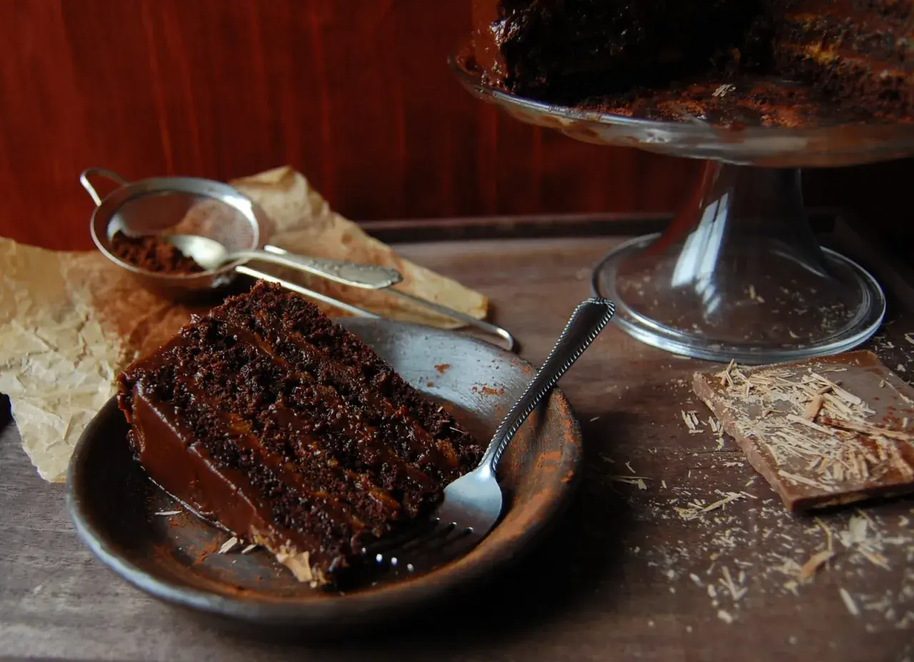 Wilgotny tort czekoladowy z kremem nutella, posypany kakao, czeka na widelca. Obok kawałek czekolady.