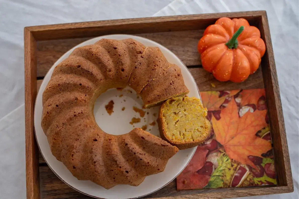 Un delicioso bizcocho de calabaza, con una porción cortada, sobre una bandeja de madera junto a una calabaza decorativa y una servilleta de hojas de otoño.